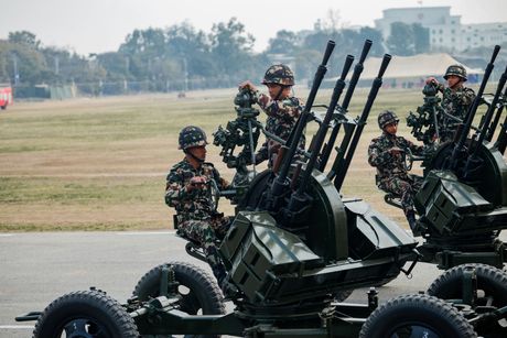 Soldiers in camouflage uniforms operate anti-aircraft machine gun emplacements on a field during a training exercise.