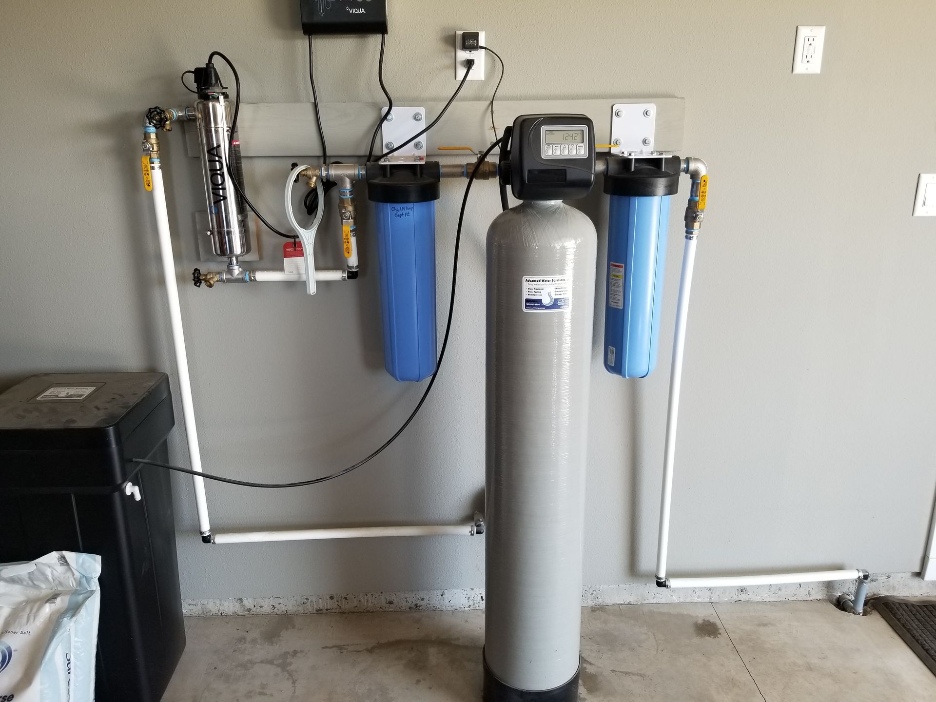 Water softener and blue filter canisters installed against a basement wall.
