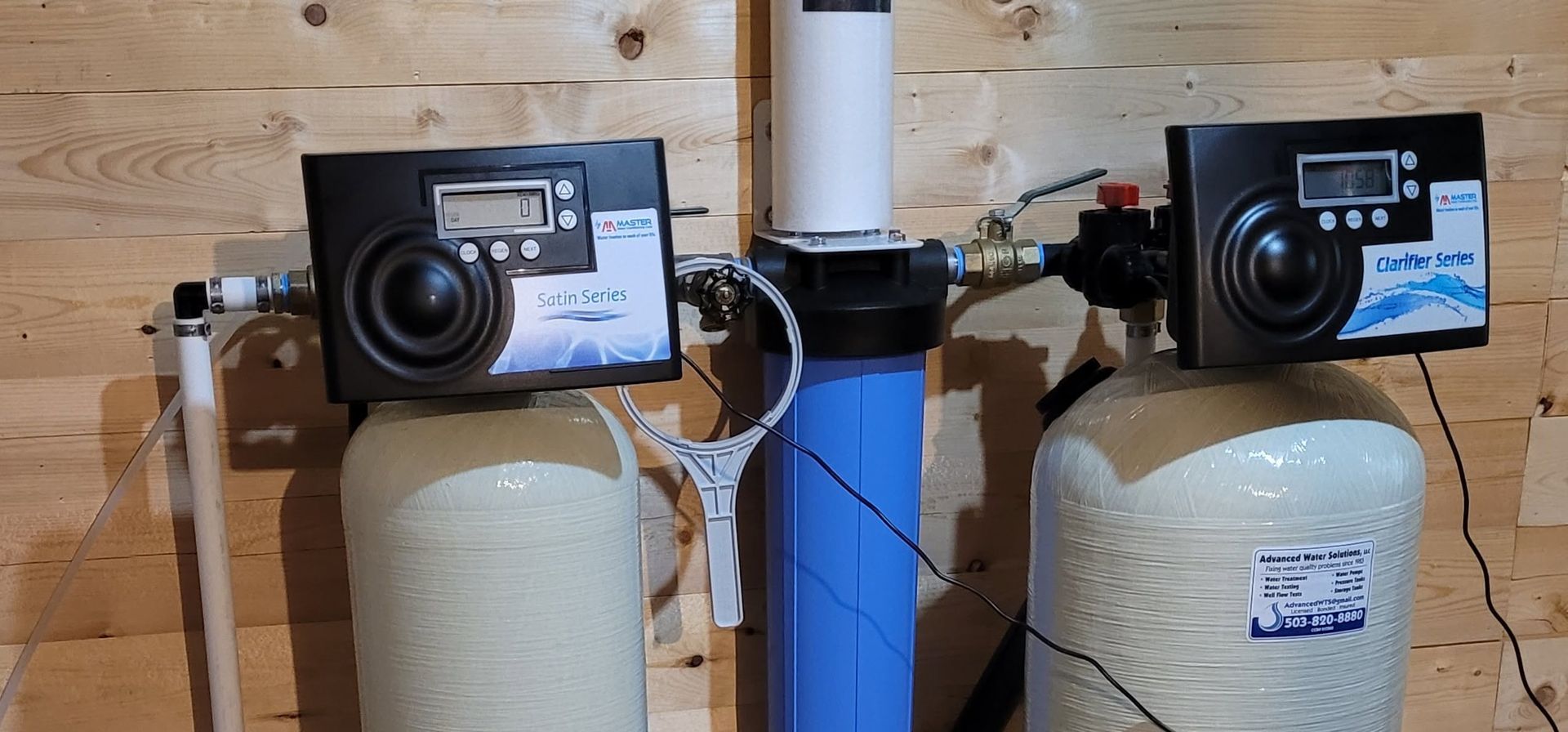 Two propane tanks with black control panels mounted on a blue pipe in a wooden shed