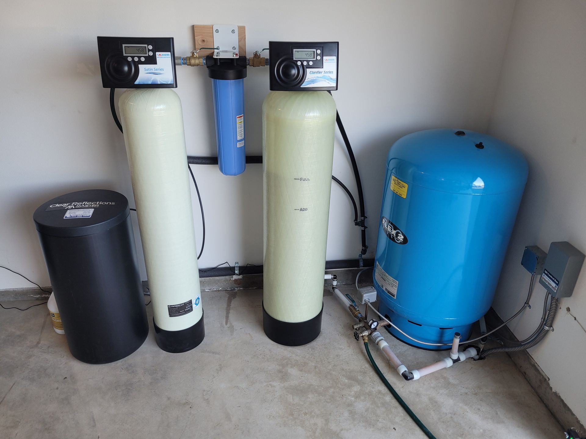 Water softener and filtration system with two tall tanks, a blue pressure tank, and a black cylinder in a utility room