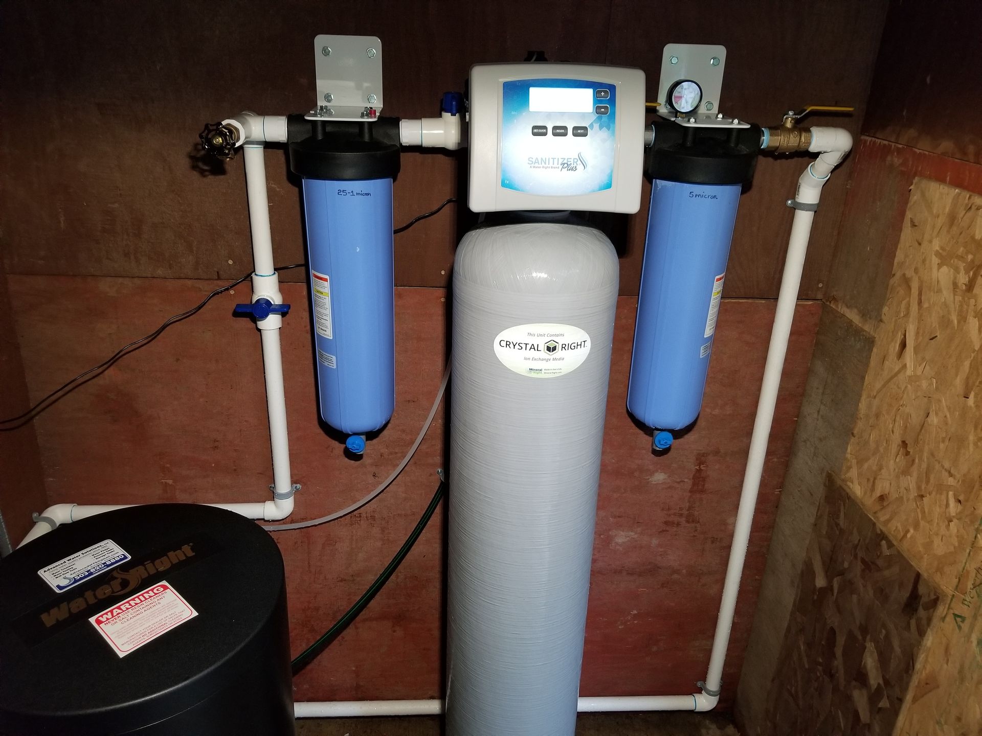 Whole-house water filtration system with blue filter tanks, control unit, and black pressure tank in a utility room