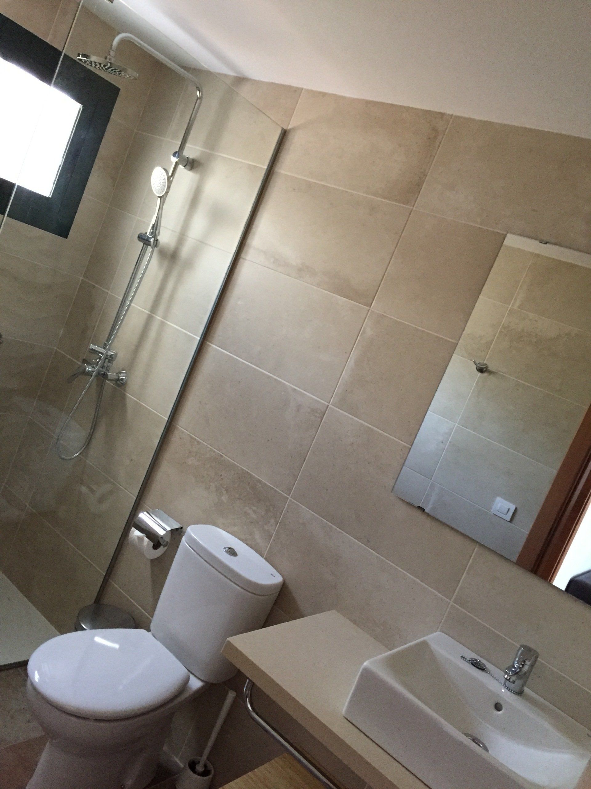 Baño con paredes de azulejos beige, ducha, inodoro, lavabo y espejo.