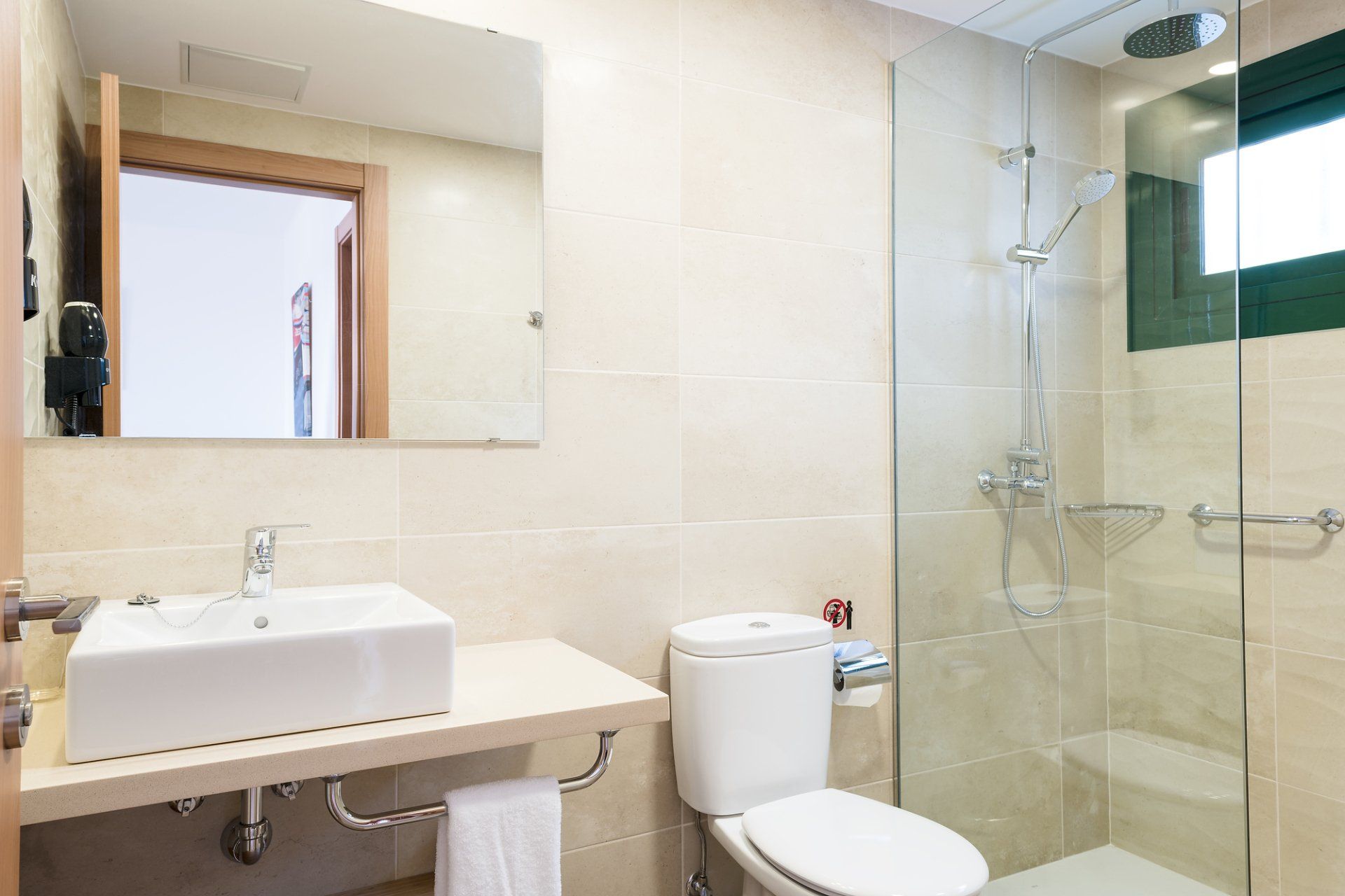 Baño moderno con lavabo, inodoro y ducha blancos. Paredes claras y espejo.