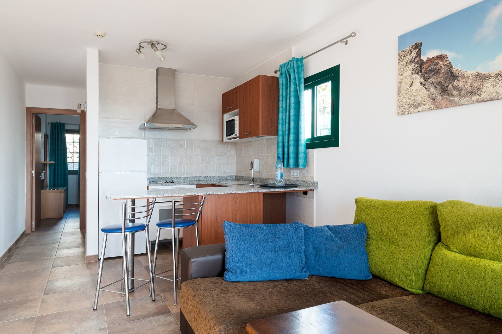 Interior de apartamento pequeño con cocina americana, sofá y mesa.