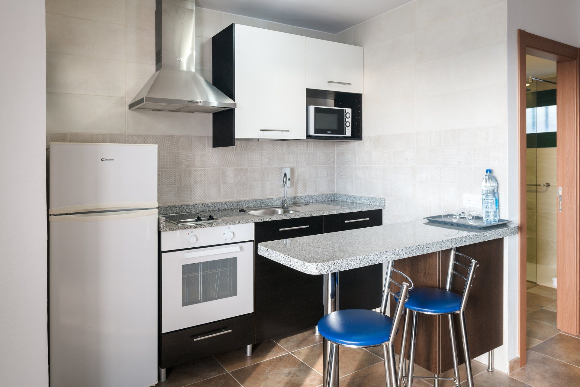 Cocina pequeña con electrodomésticos blancos, gabinetes en blanco y negro y barra de desayuno con taburetes.