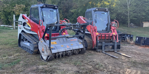 Two red tracked forestry mulcher machines parked in a muddy clearing