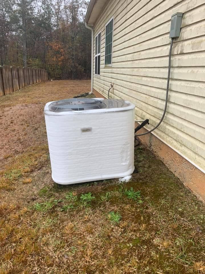 An outdoor residential air conditioning unit sits on the grass beside a house with beige siding.