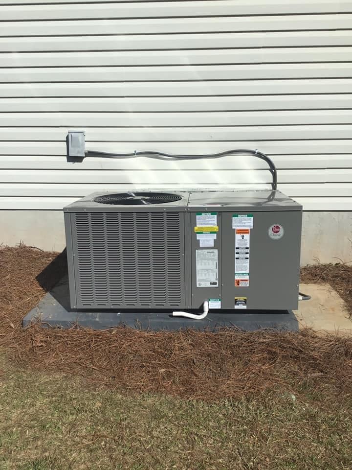 A grey outdoor air conditioning unit sits on a concrete pad against white vinyl house siding.