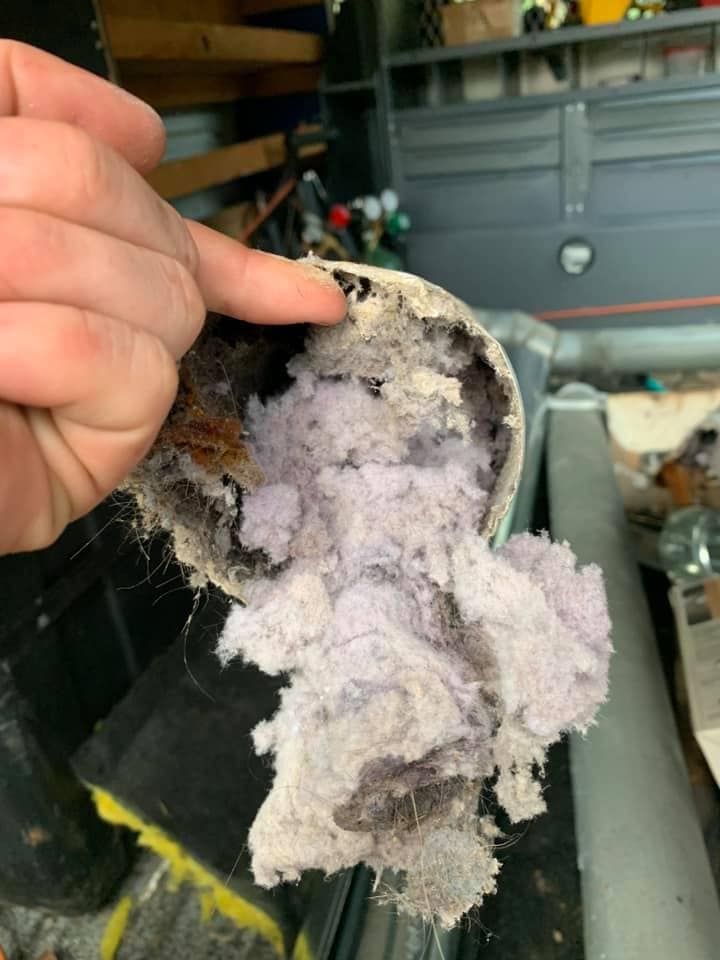 A person holds a section of pipe packed tightly with gray, fibrous material and debris.