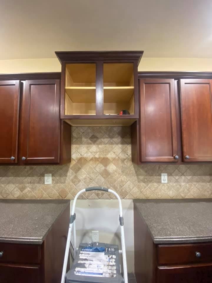 A kitchen counter with a step ladder placed below an open, dark wood cabinet flanked by matching closed cabinets.