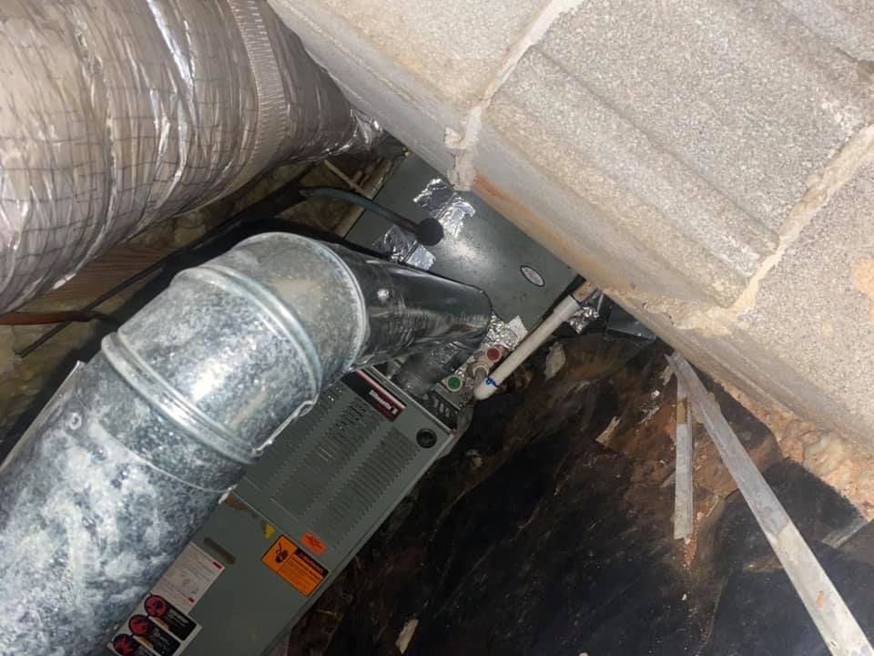 An HVAC unit located in a crawl space, featuring silver metal ductwork, grey metal casing, and surrounding insulation.