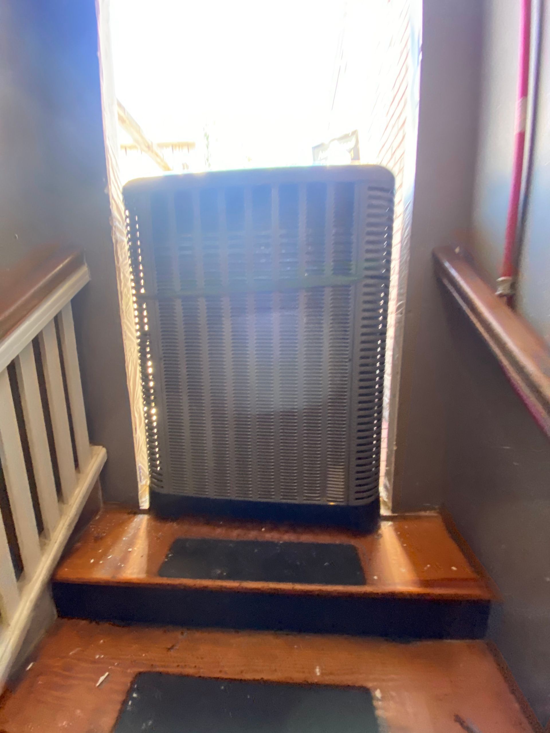 A large, gray air conditioning unit sits on the landing of a wooden staircase, blocking access to the doorway.