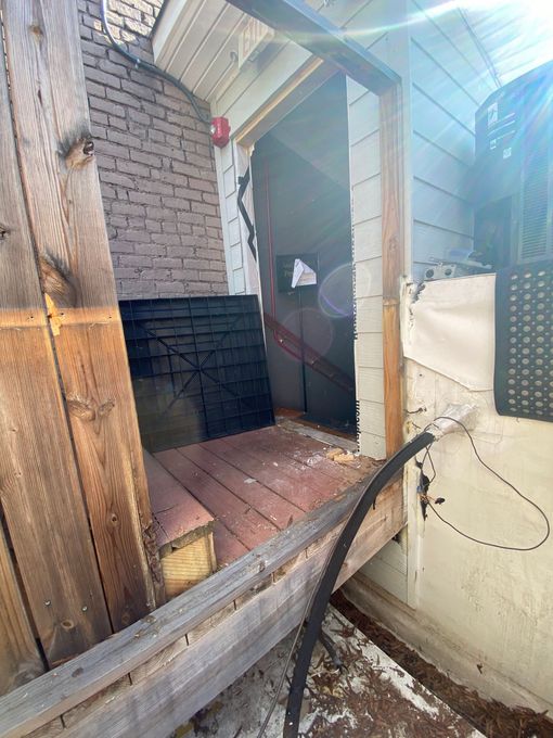 A low-angle view of a wooden porch entrance showing a missing door, weathered wood, exposed brick, and a black cable.