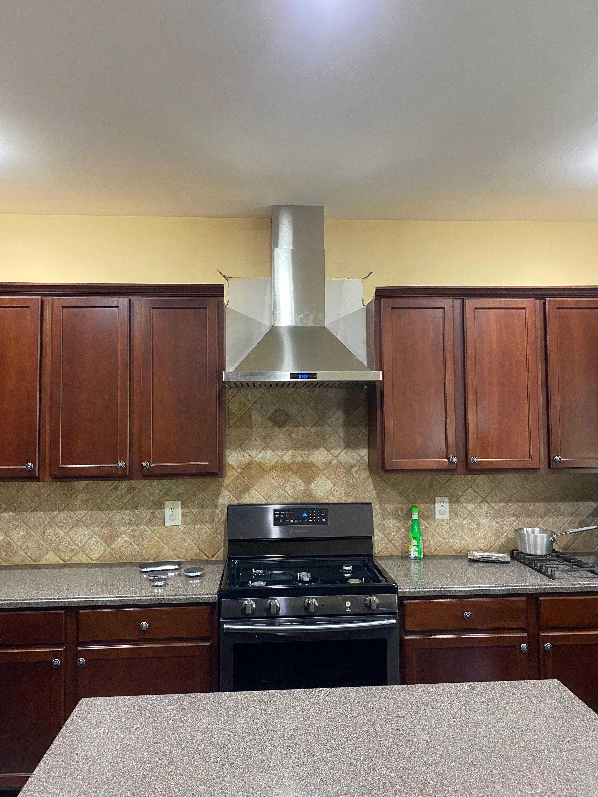 A kitchen with dark wood cabinets, a stainless steel range hood, a black gas stove, and a granite countertop.