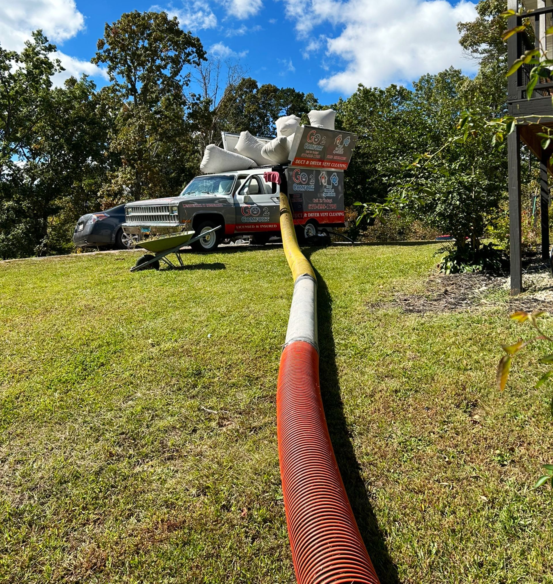A specialized service truck with filtration bags parked on grass, connected to a long, red hose extending toward the viewer.