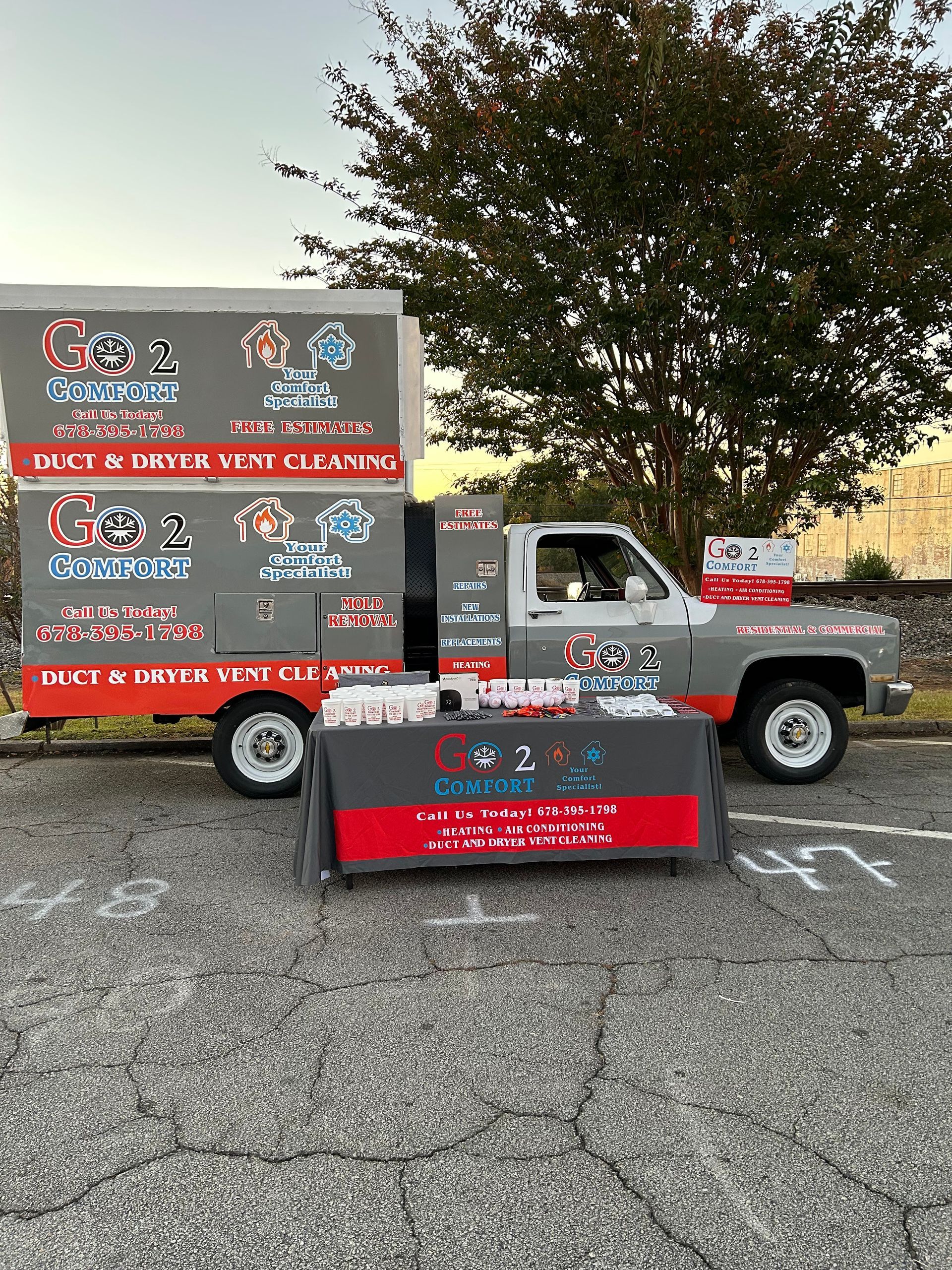 A grey work truck and a branded promotional table set up in a parking lot for Go 2 Clean, a cleaning service.
