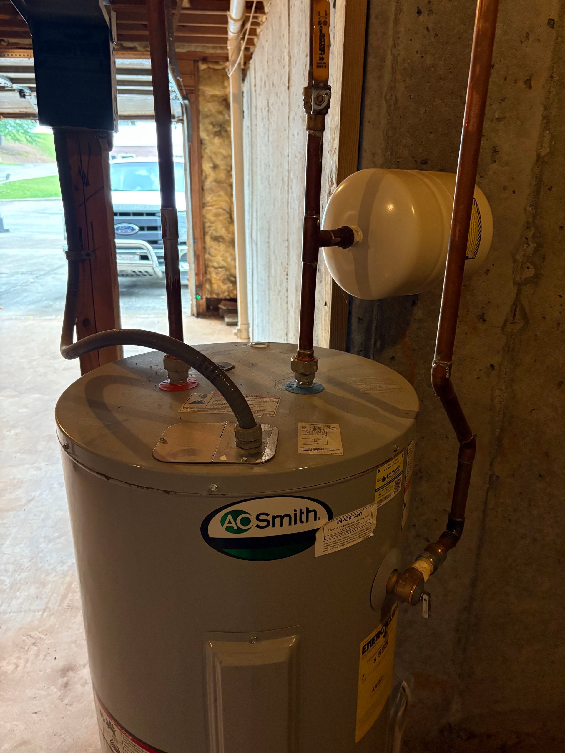 An A. O. Smith water heater in a basement with copper piping and a white thermal expansion tank attached.