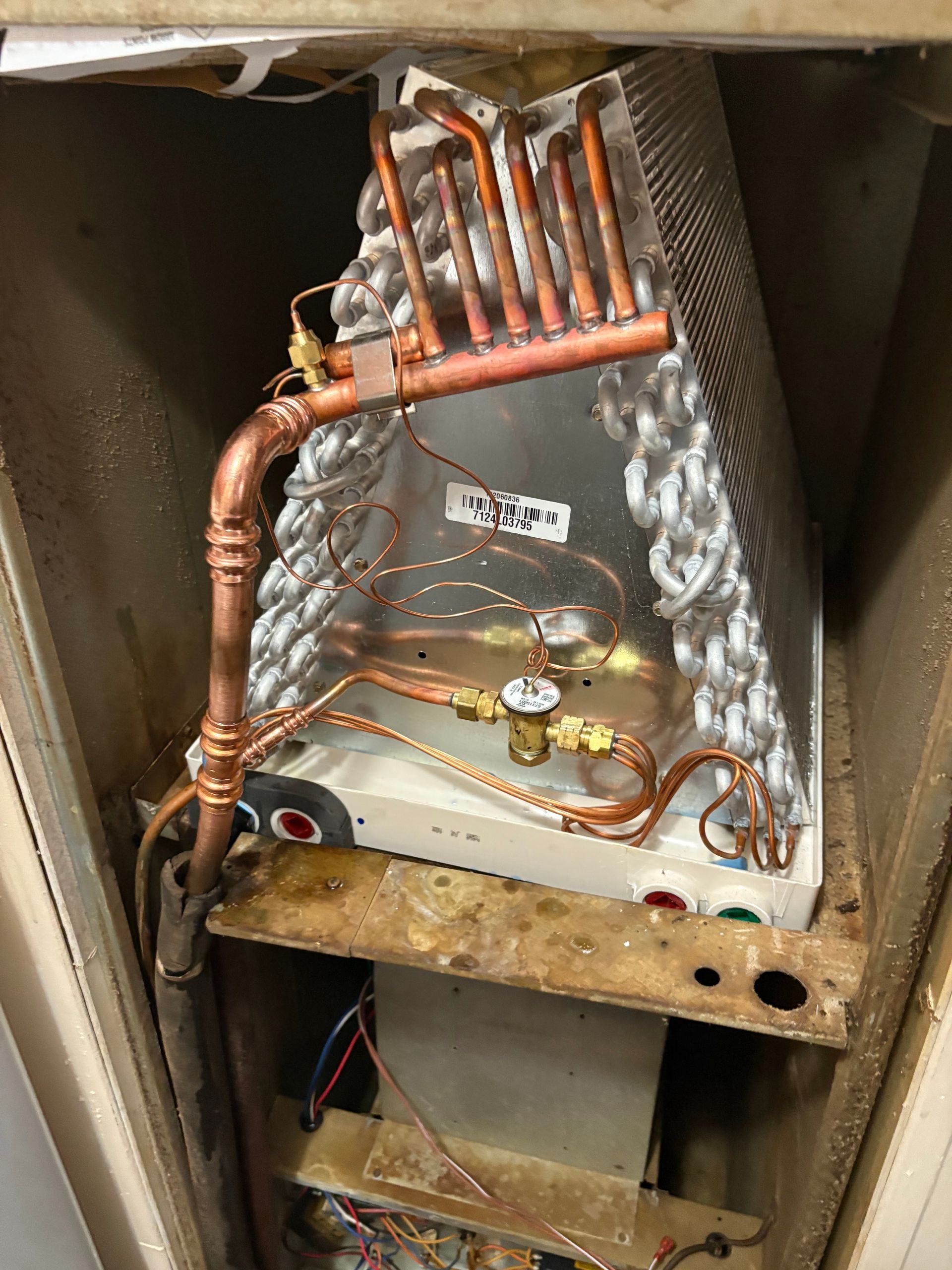 An indoor air conditioning A-frame evaporator coil unit inside a furnace cabinet, showing copper tubing and components.