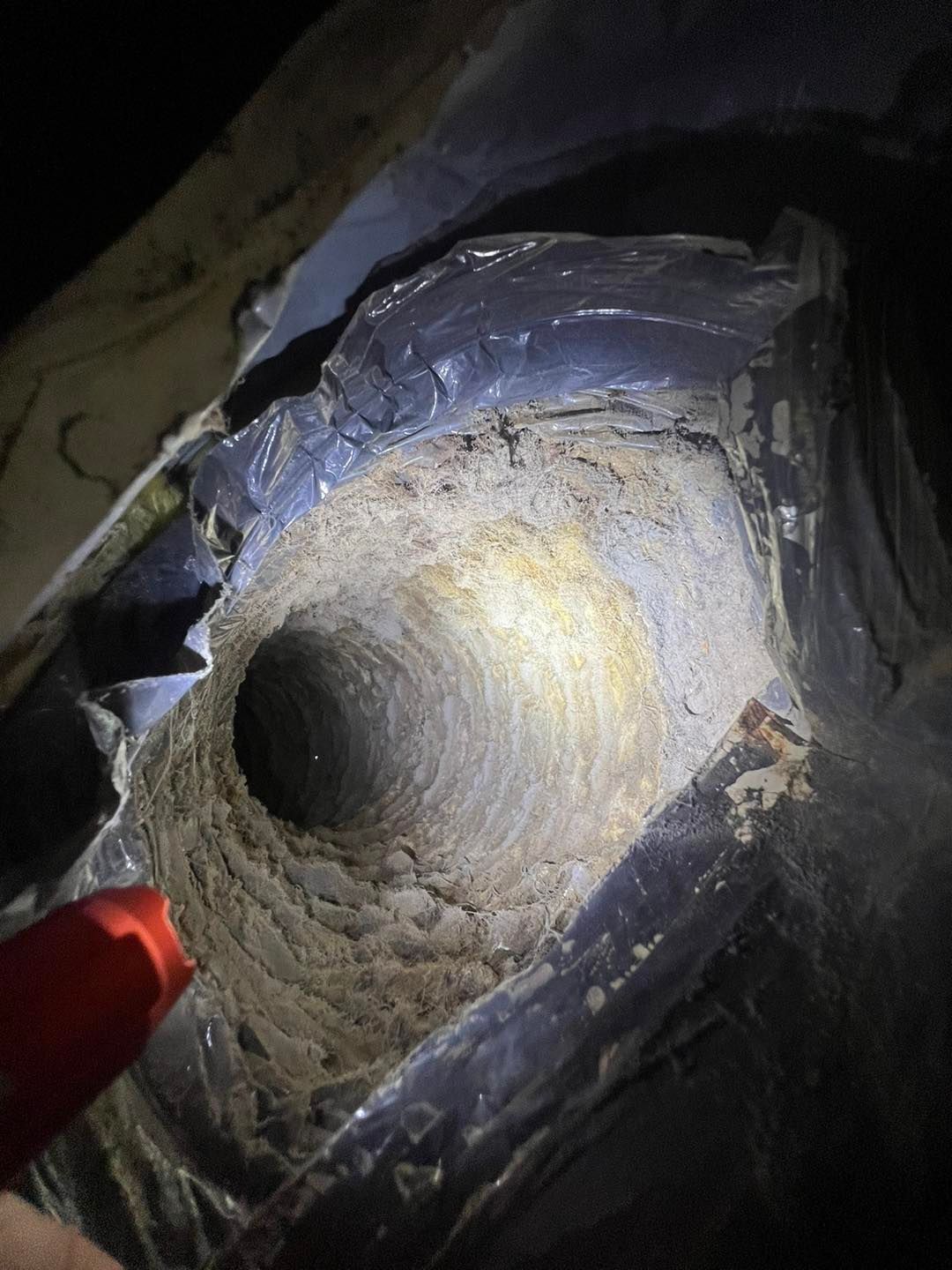 A flashlight illuminates the heavily dust-coated interior of a flexible residential HVAC duct.