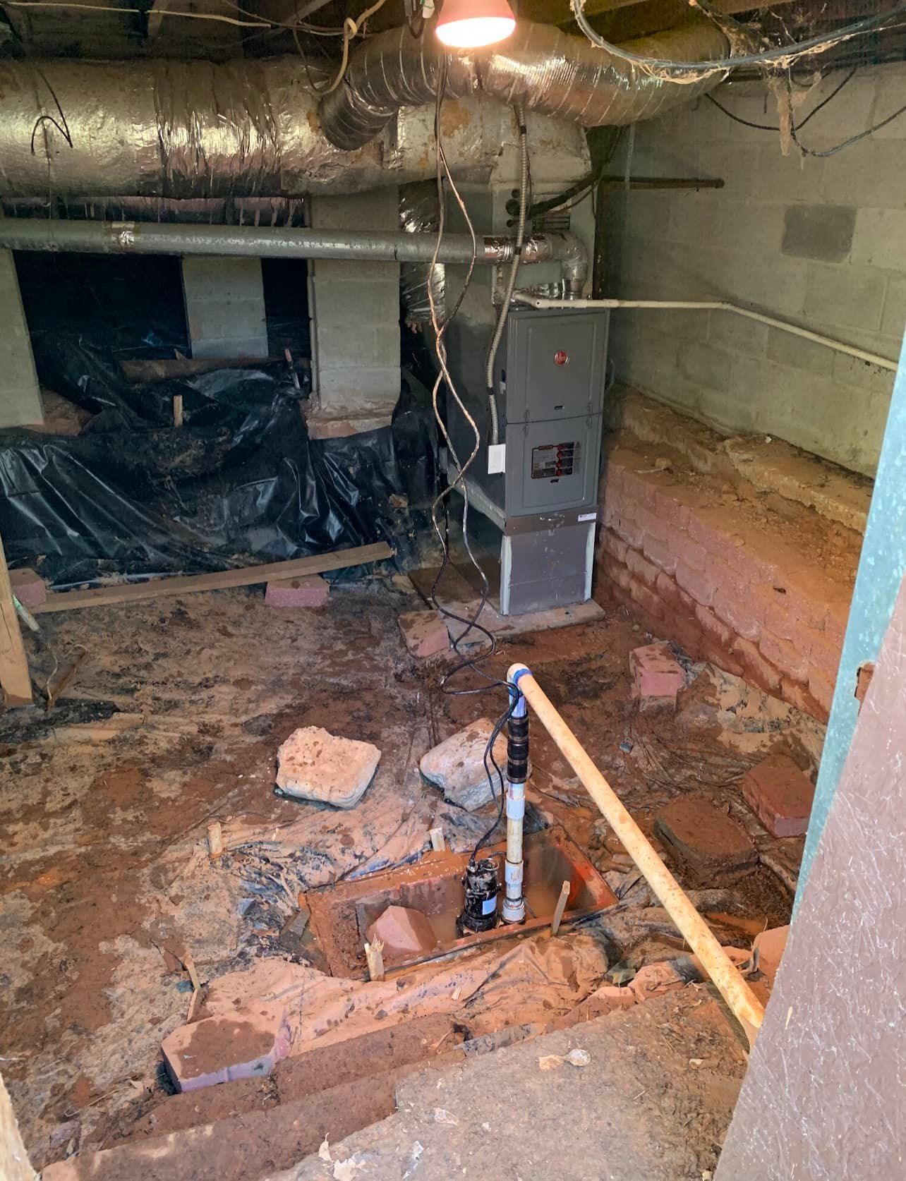 A crawl space with a dirt floor, a central sump pump, and a gray furnace unit under metallic ductwork.