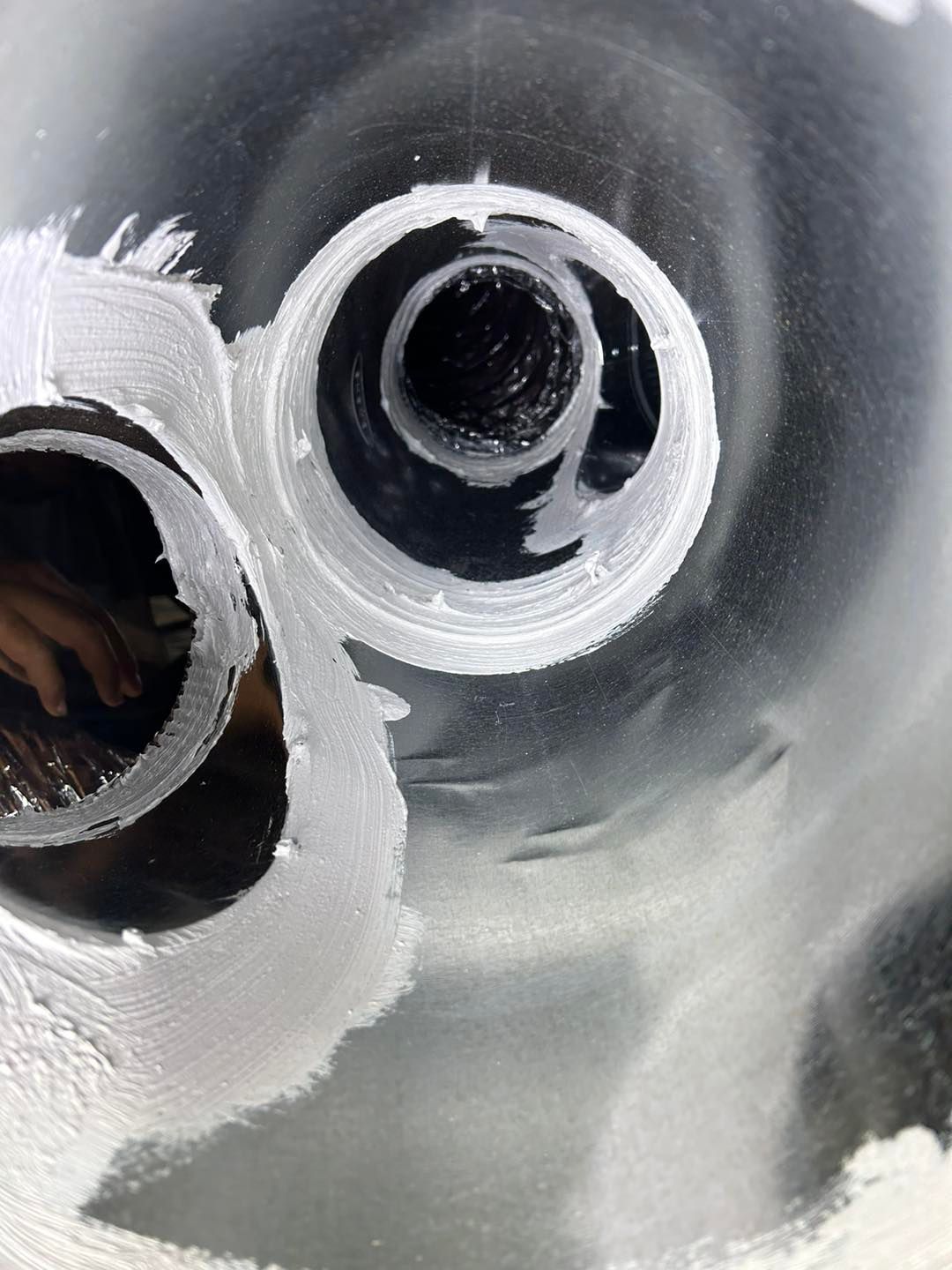 Close-up of two circular holes cut into a black surface, surrounded by rough, white residue or sealant.