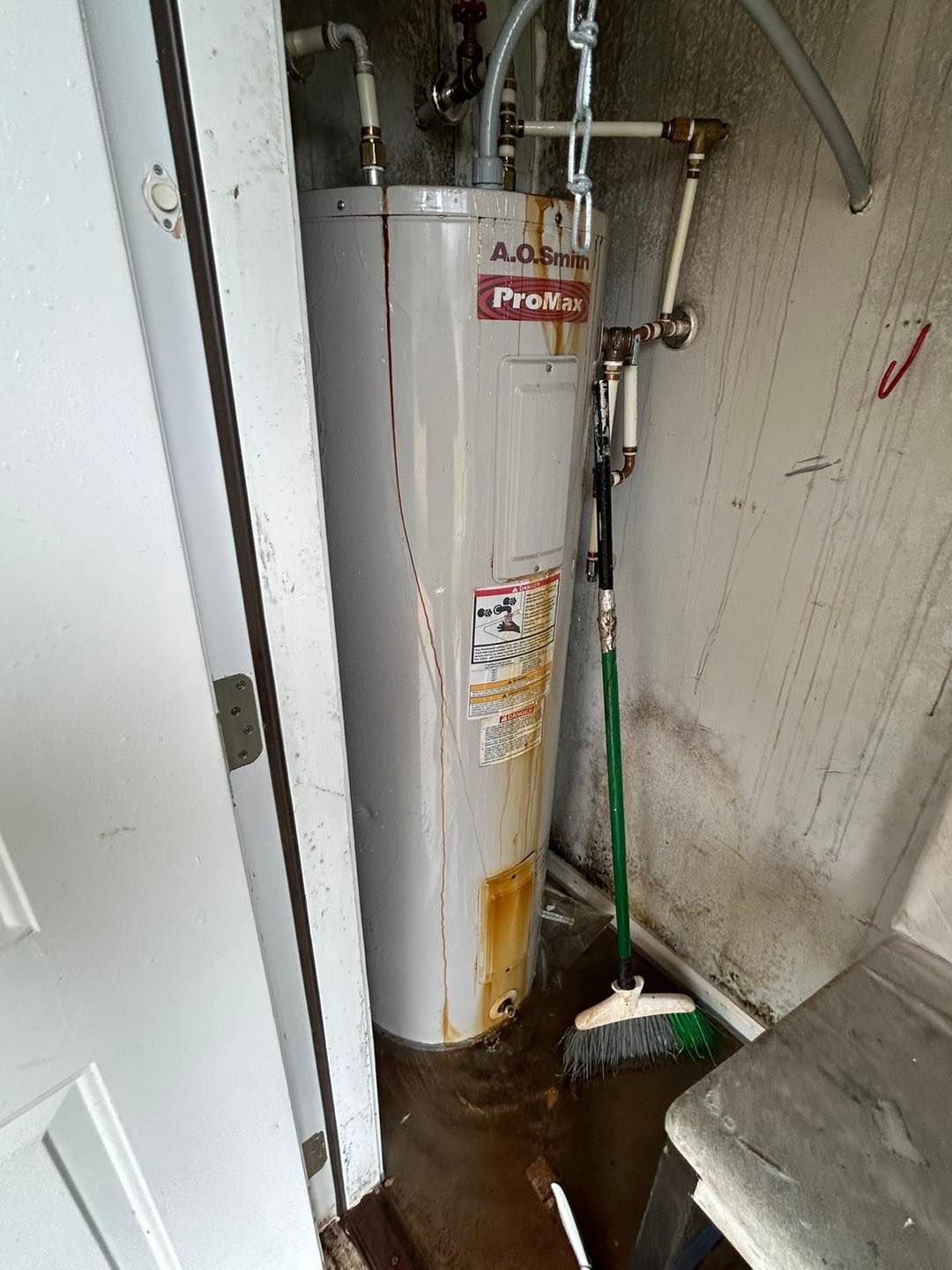 A leaking water heater stands in a closet, showing significant rust stains and pooling water on the floor.