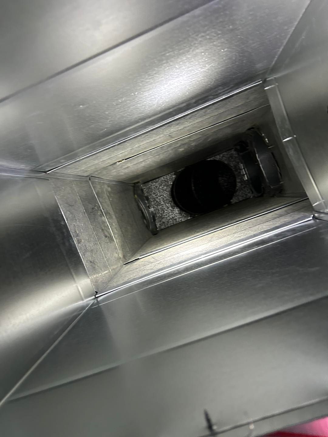 A view looking down into a rectangular metal air duct, showing a dark, circular opening at the far end.