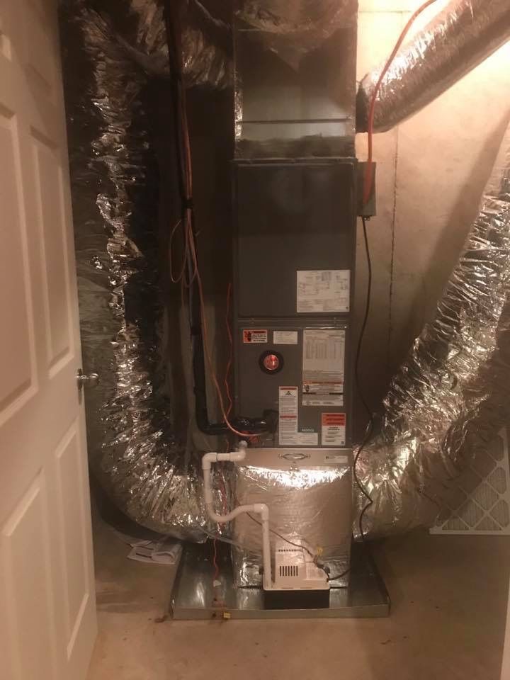 A central heating and cooling air handler unit in a closet, connected to large silver insulated flex ductwork.