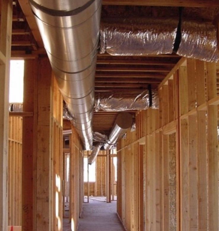 A hallway under construction with exposed wooden framing and metal HVAC ducts installed between the ceiling joists.