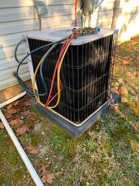 An outdoor residential HVAC condenser unit with colorful pressure gauge hoses attached, sitting on a concrete pad.