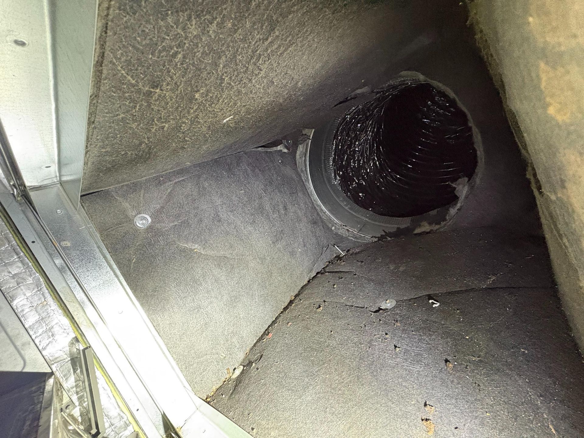 Dusty metal duct with a round black vent opening inside an HVAC vent