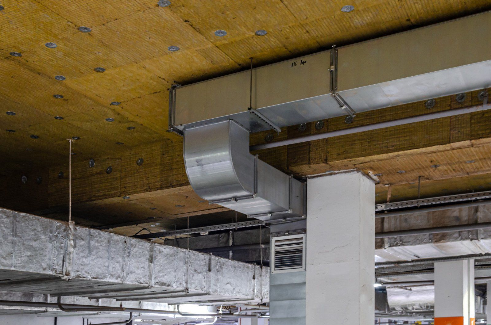 Exposed ventilation ductwork and ceiling insulation in an industrial or underground parking structure.