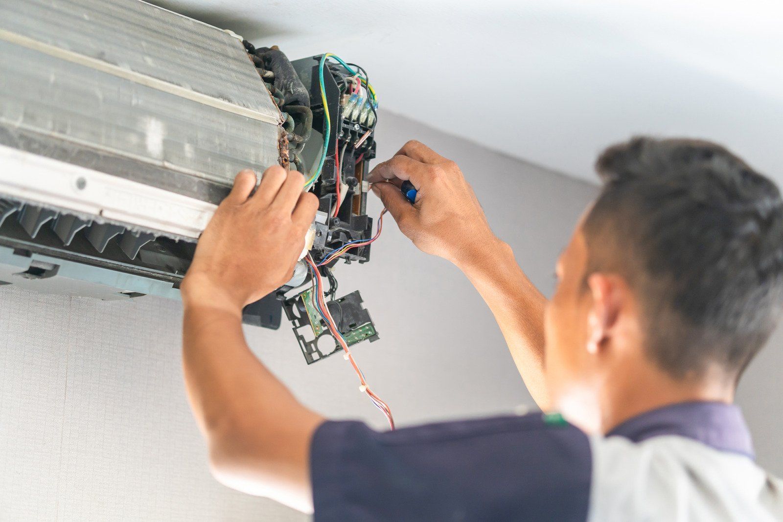 A technician repairs the exposed internal wiring of a wall-mounted air conditioning unit.