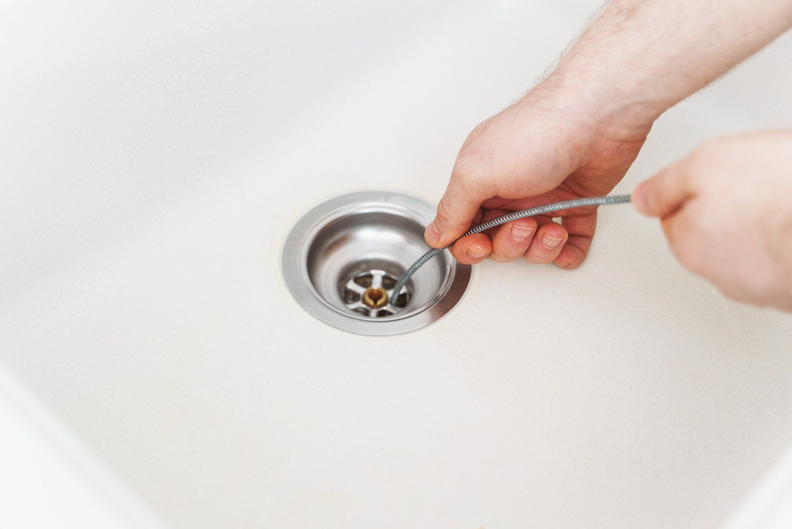 A person uses a flexible drain cleaning tool to clear a clog in a white kitchen sink.