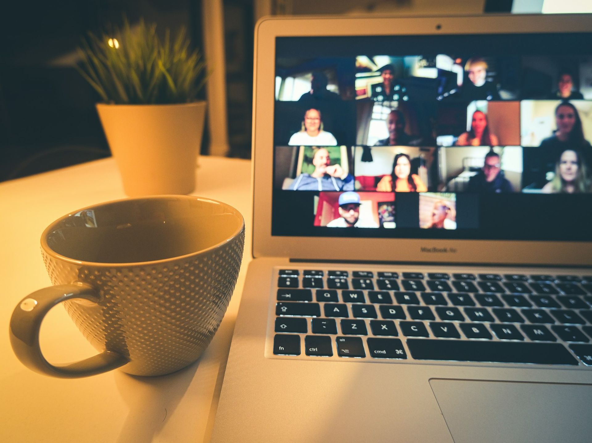 A laptop showing a video call beside a coffee cup