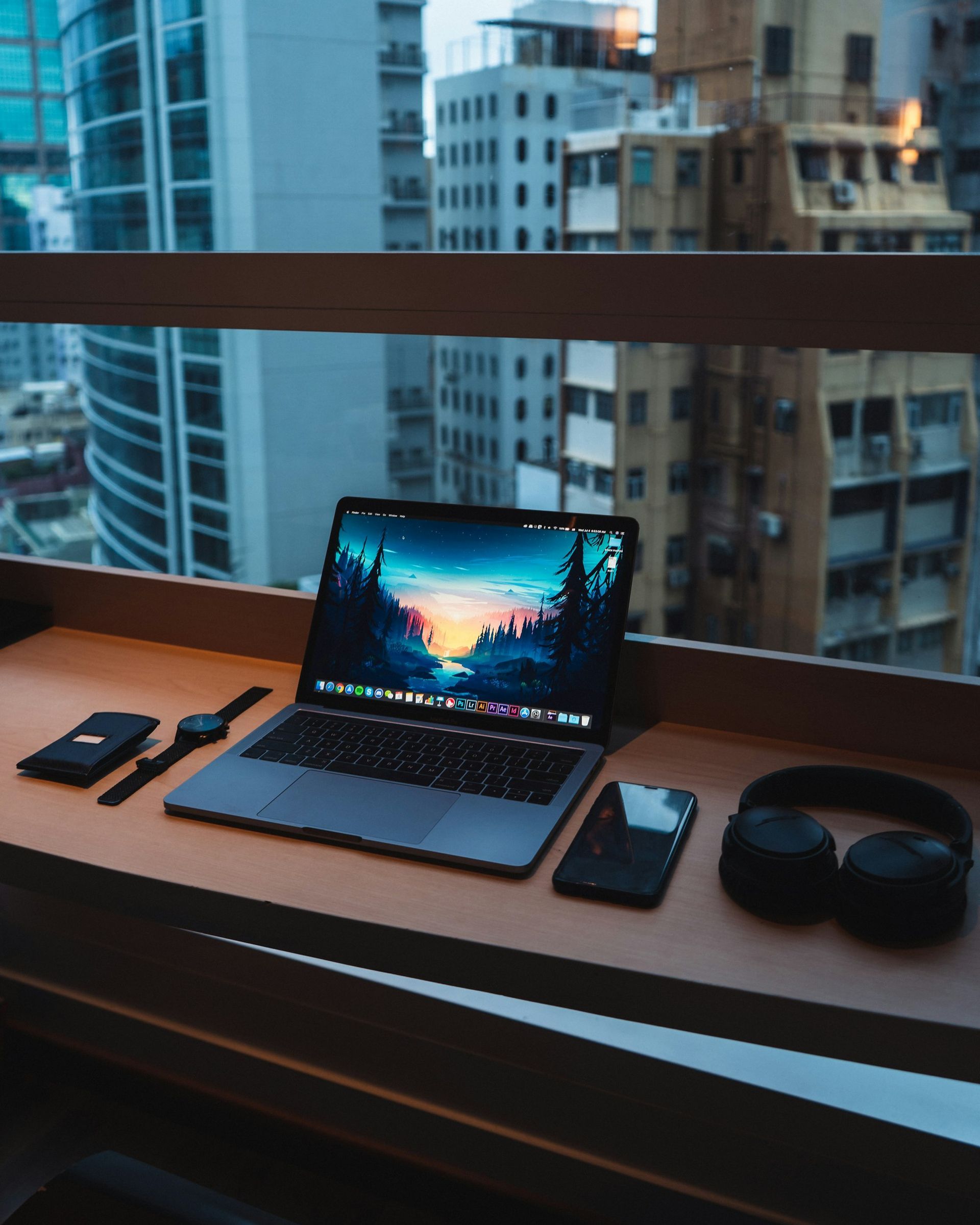 A laptop and a phone on a desk by a window