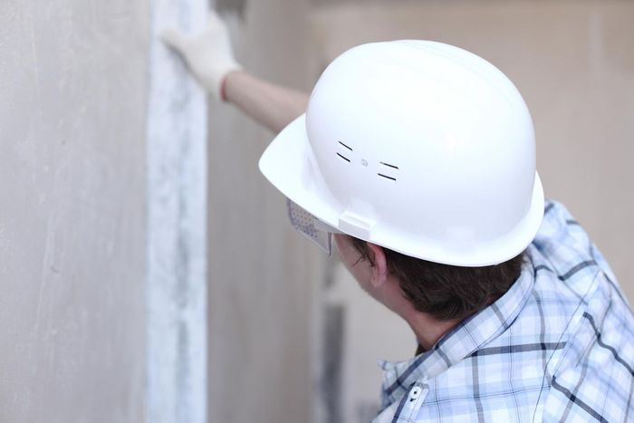 a man wearing a hard hat and safety glasses is plastering a wall