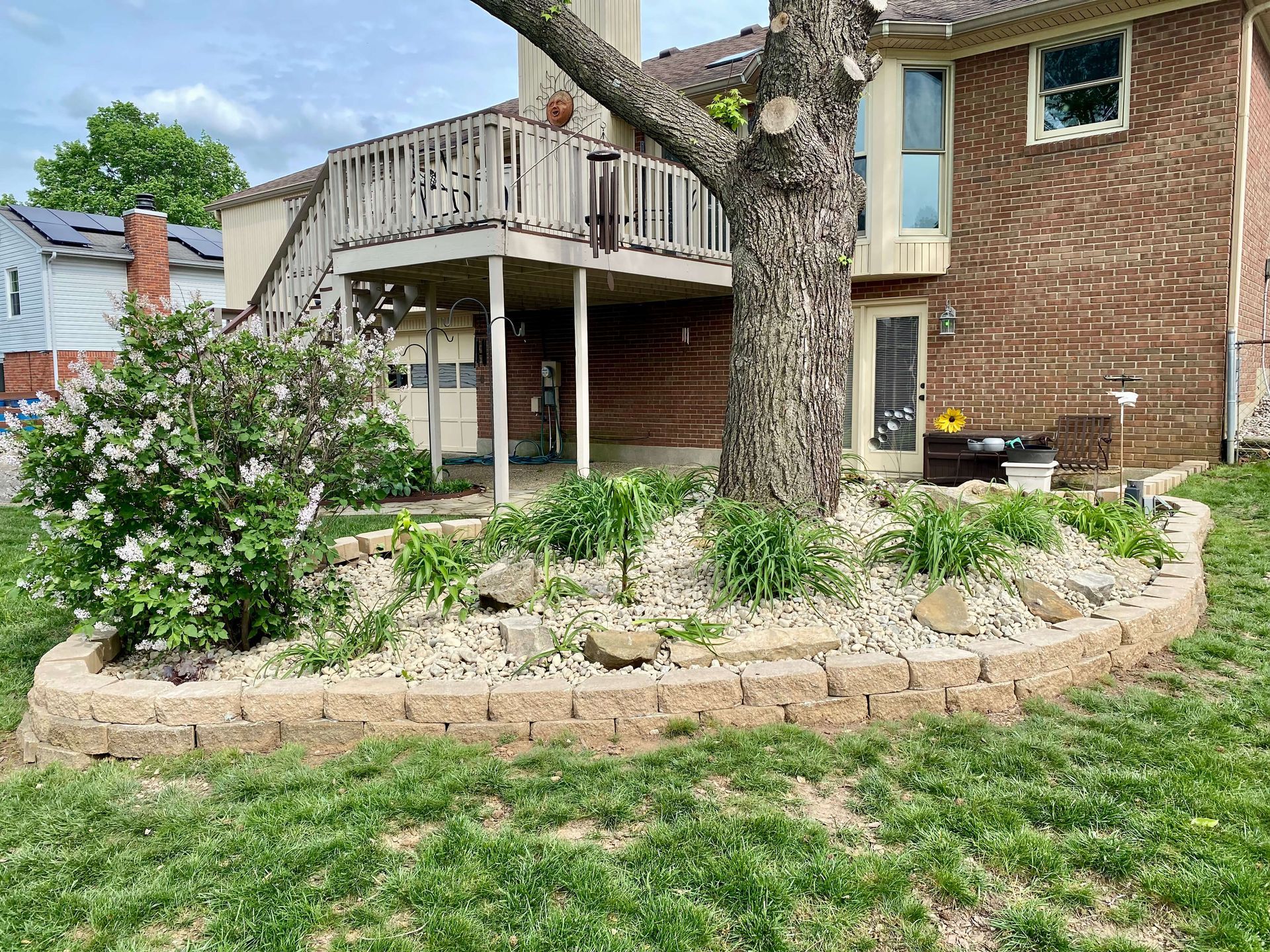 Backyard with a brick house, wooden deck, tree, and landscaped garden bed