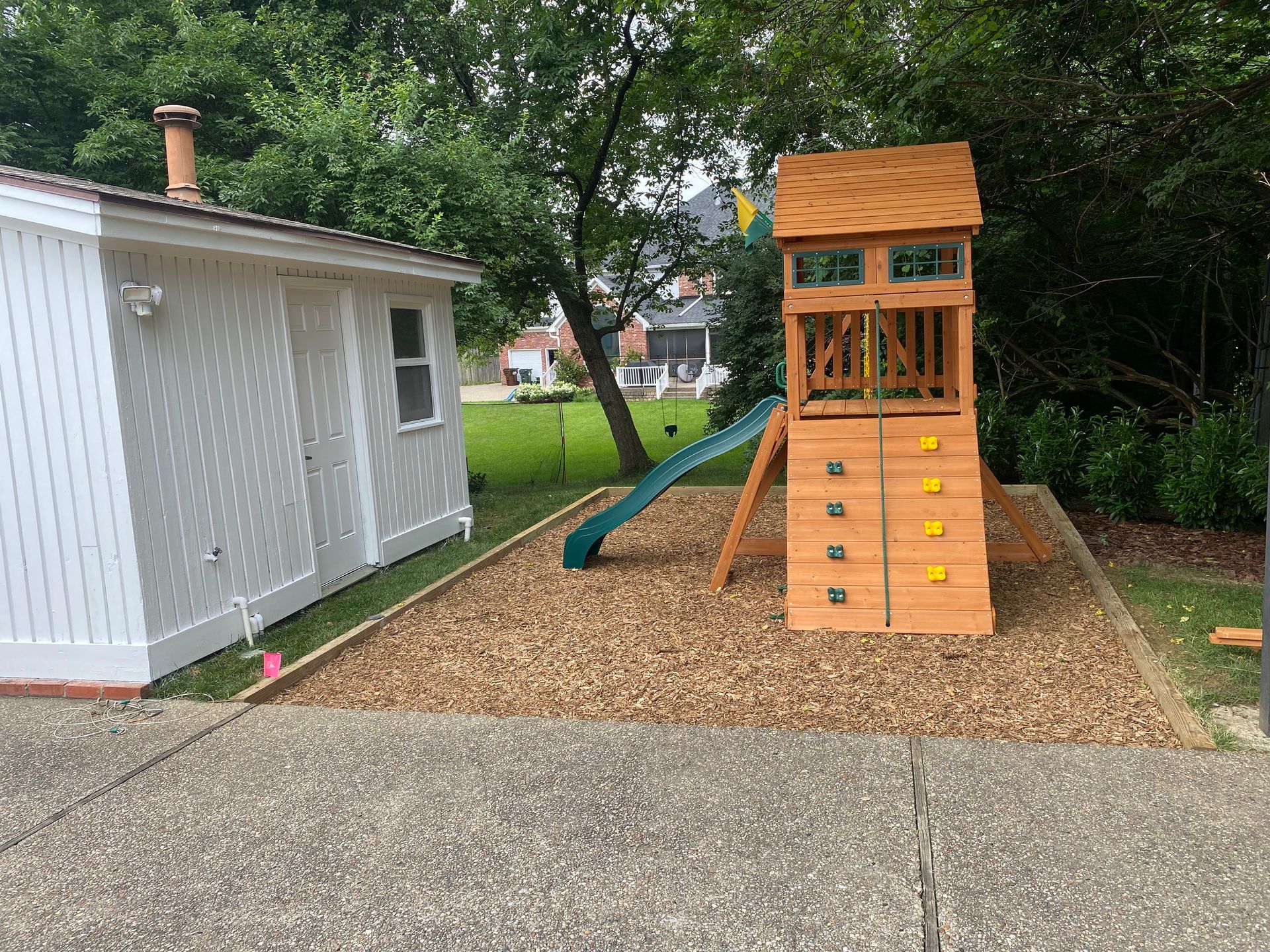 Play structure with a slide and climbing wall in a yard next to a white shed.