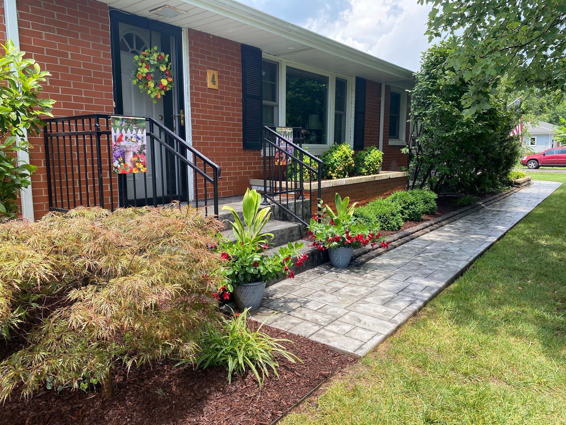 Brick house front porch with hanging wreath, flower beds, and a stone walkway leading to the entrance