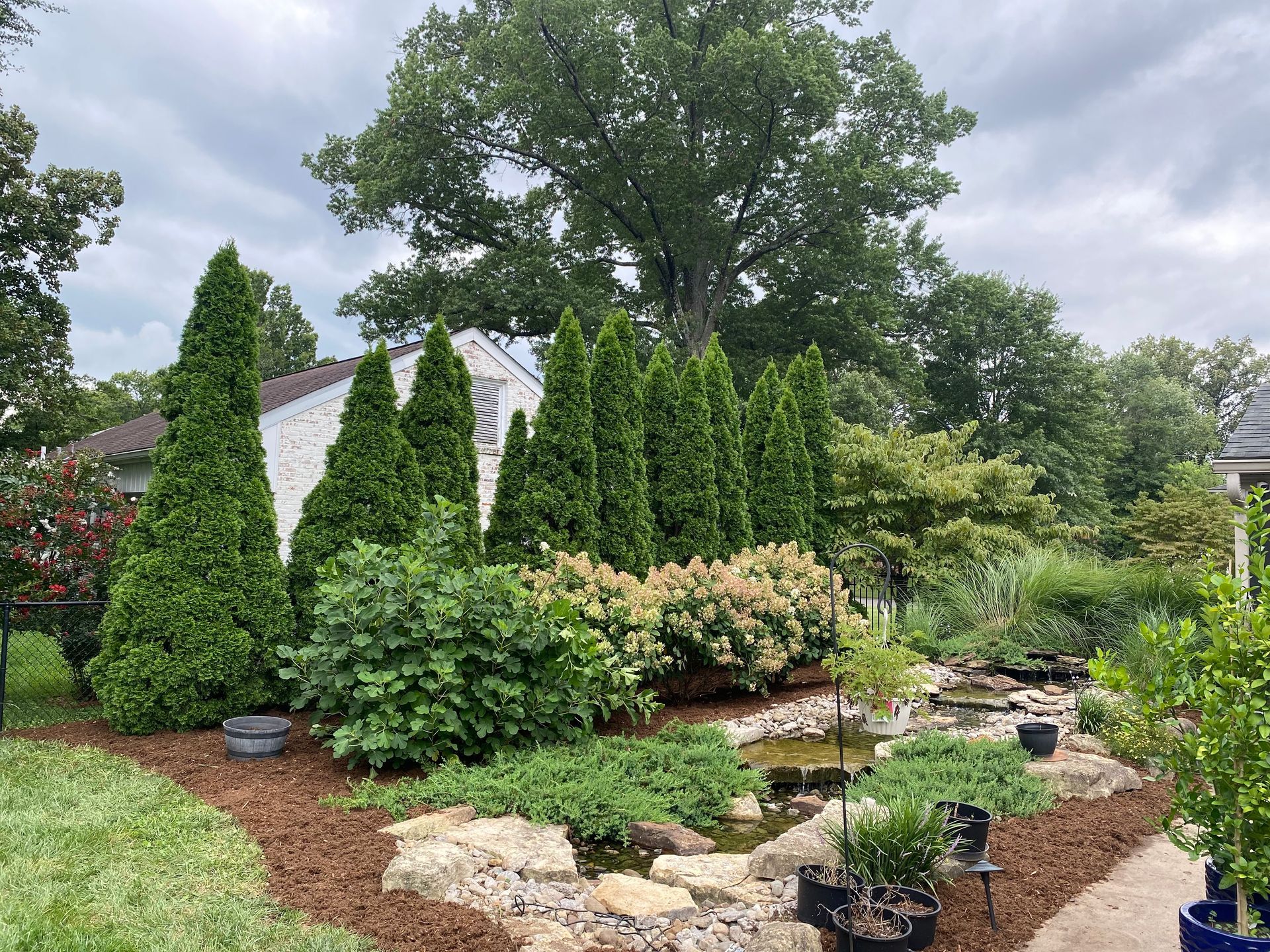 Landscaped garden with evergreen shrubs, flowering bushes, and a stone-lined pond path