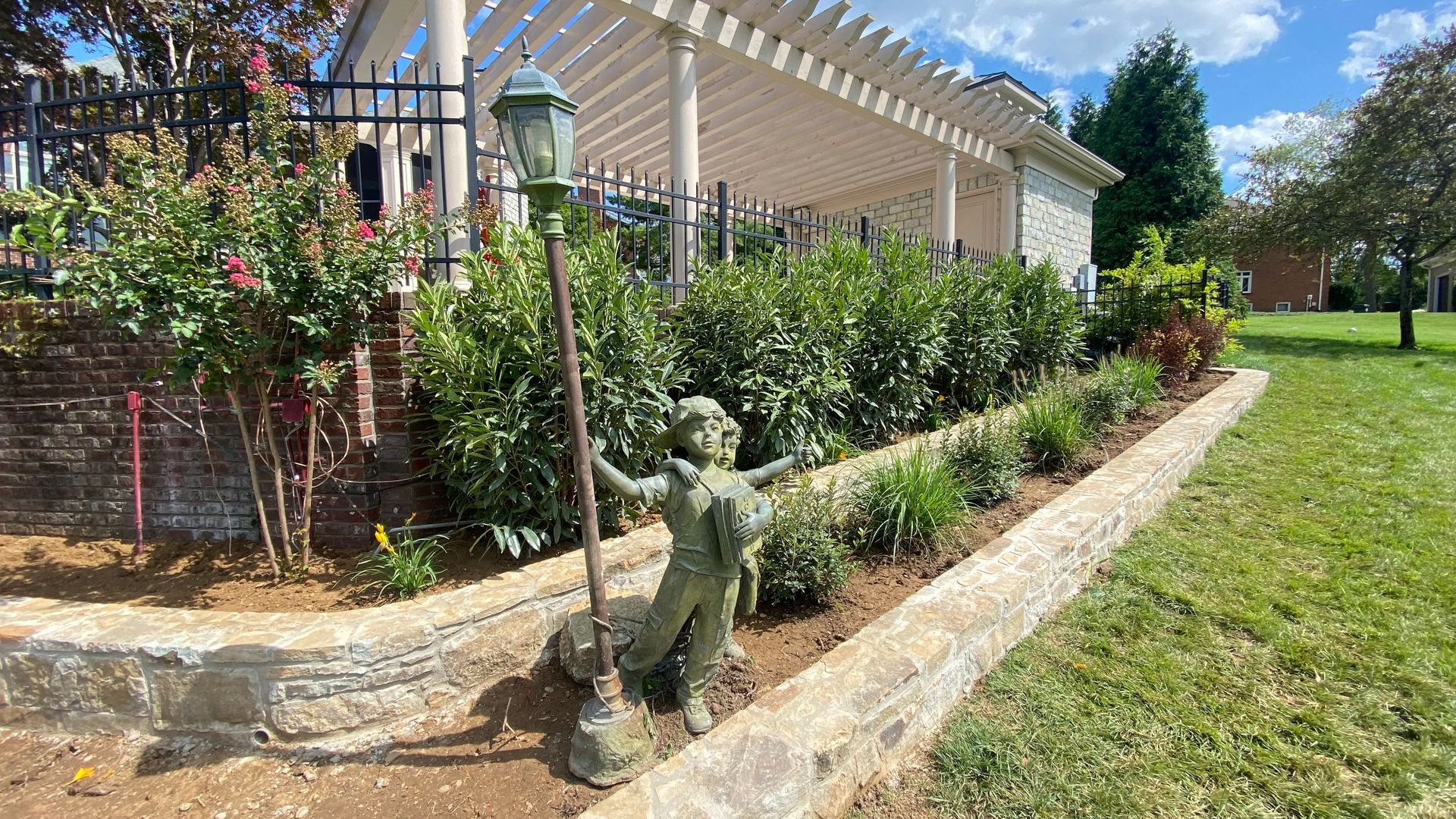 A statue of a child holding a lamp post in a landscaped area next to a building.