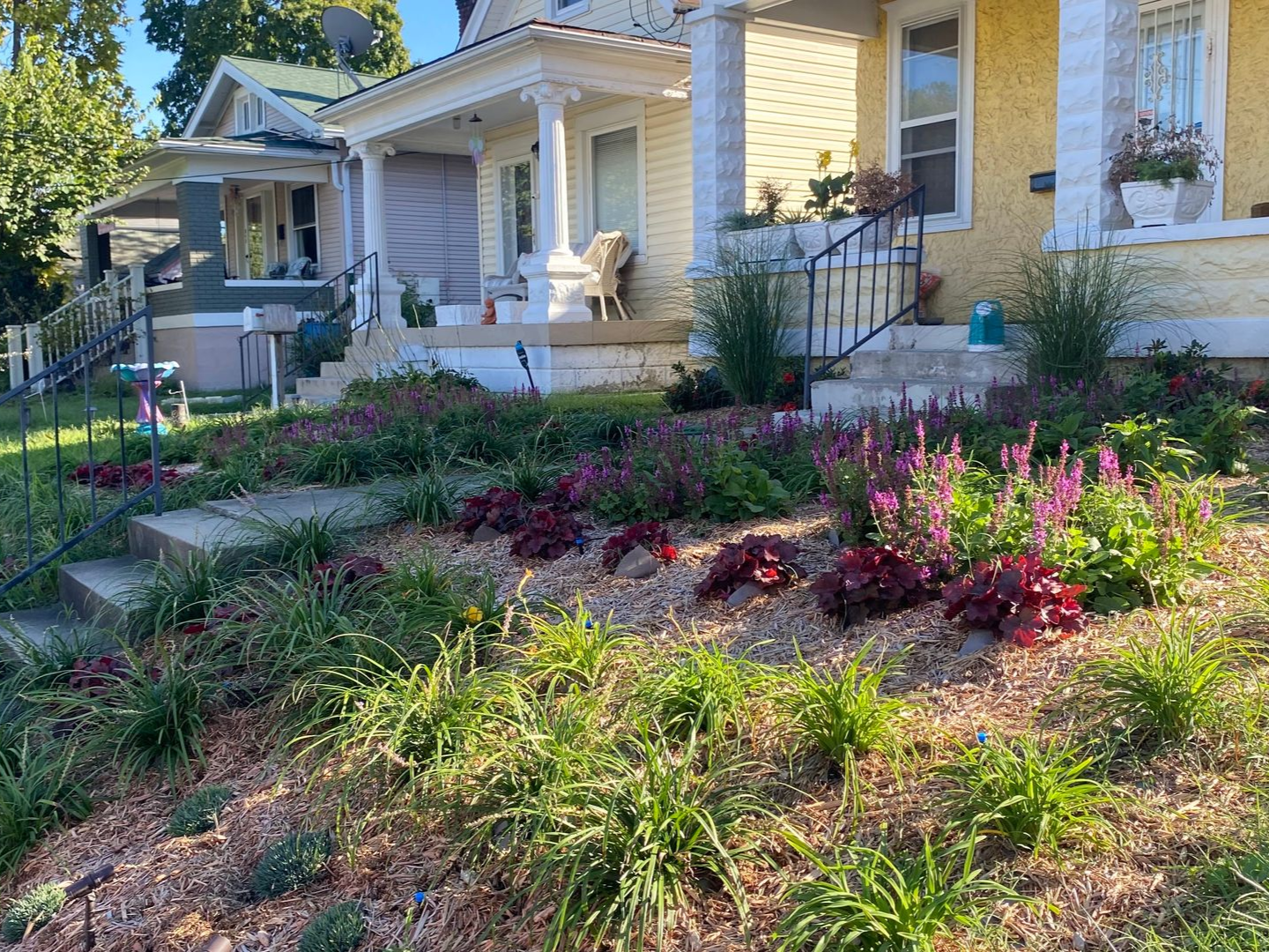 Front yard garden with pink flowers and a yellow house porch at dusk