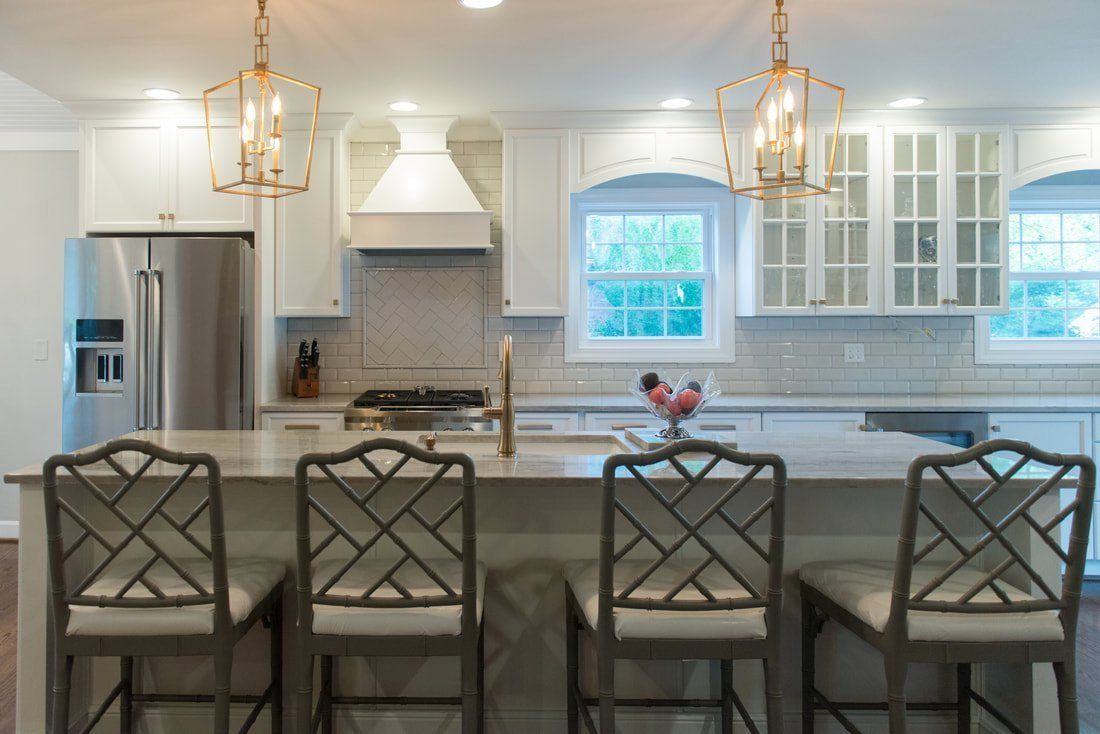 Modern white kitchen with island seating, pendant lights, stainless steel appliances, and bright windows.