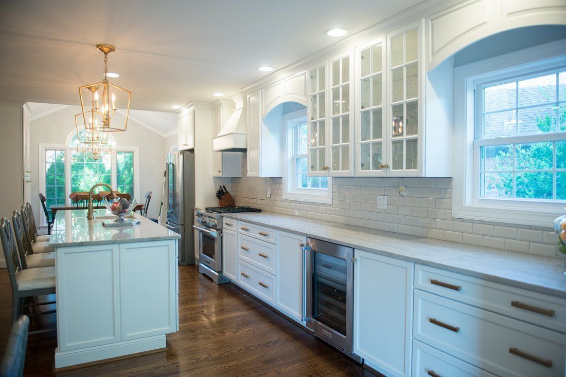 Bright white gourmet kitchen with island, marble counters, glass cabinets, and large windows