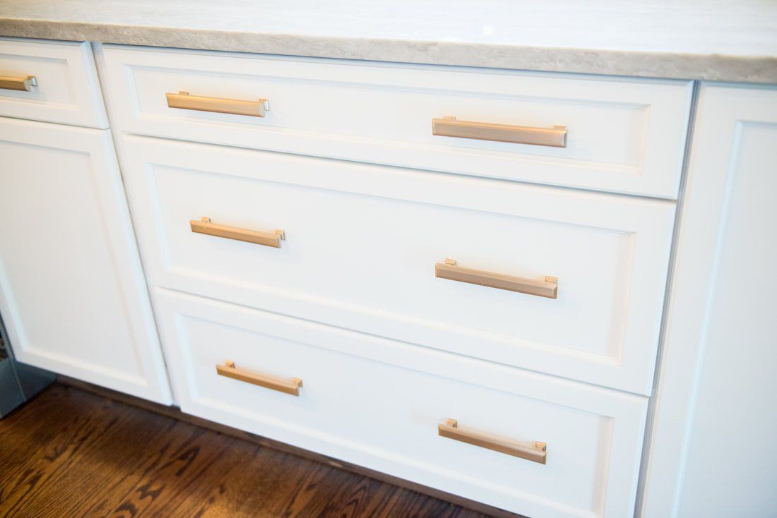 White kitchen cabinet with three drawers and wood handles over a hardwood floor