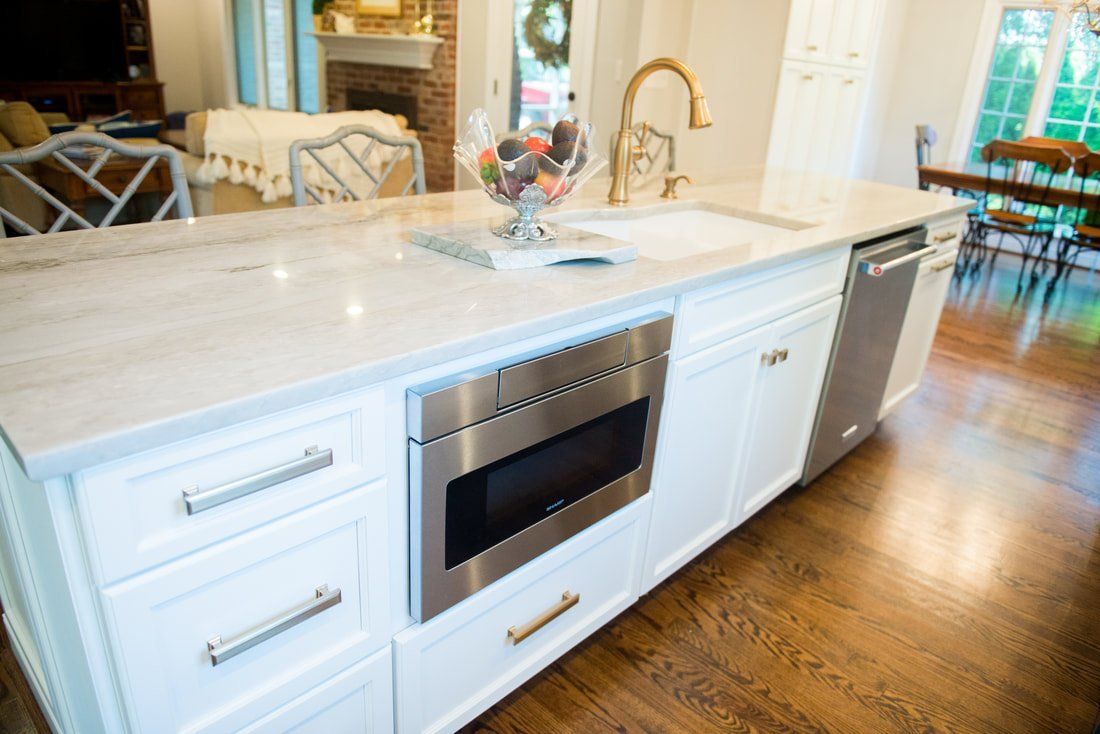Bright kitchen island with white cabinets, stainless oven, marble countertop, and hardwood floor