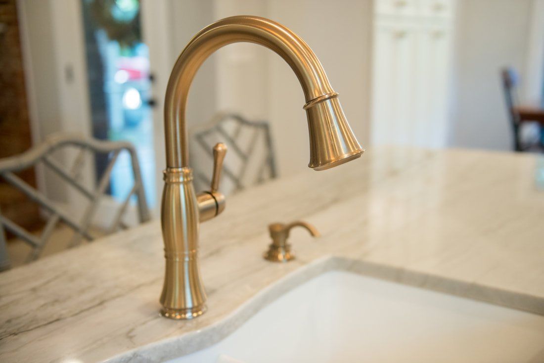 Brass kitchen faucet over a white sink on a light countertop.