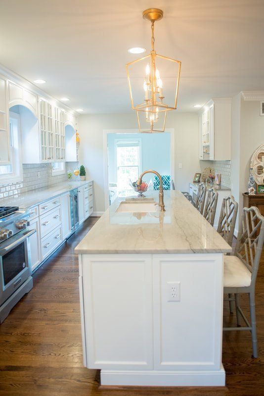 Bright white kitchen with a large island, pendant lights, stainless appliances, and wood floors.
