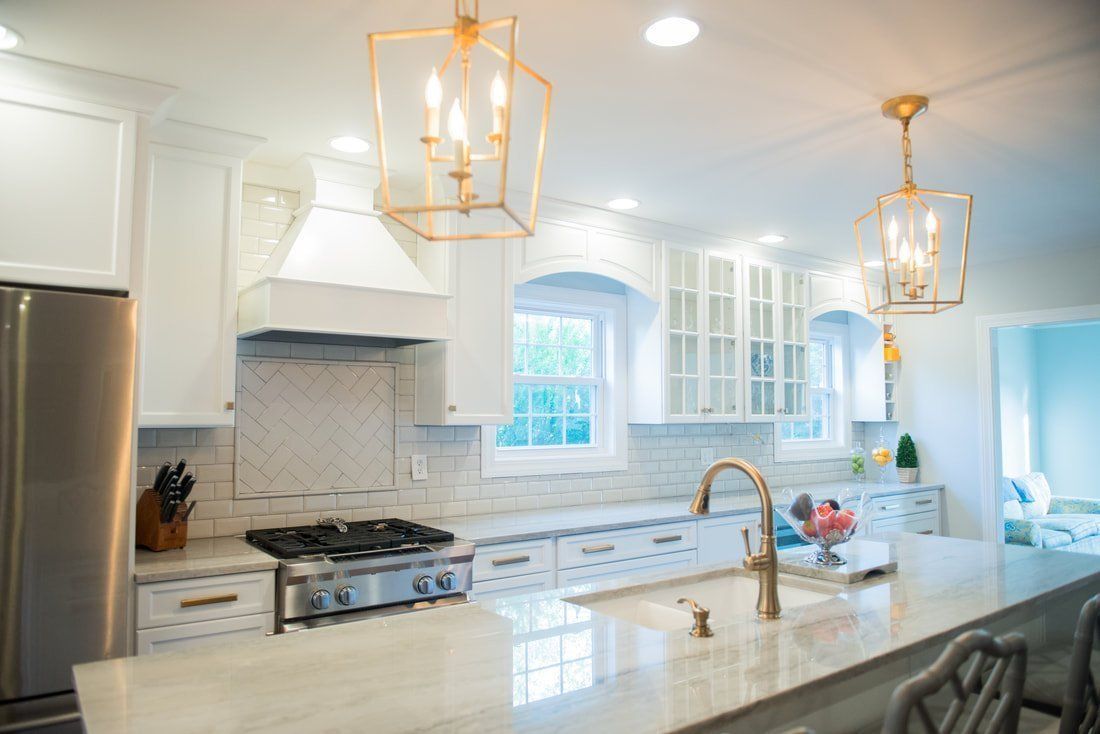 Bright white kitchen with marble island, gold pendant lights, stainless appliances, and a windowed cabinet